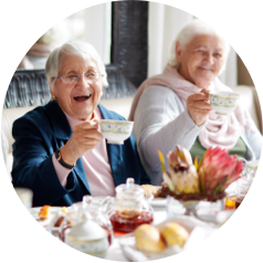 Elderly women enjoying tea together at a beautifully set table with pastries and flowers.