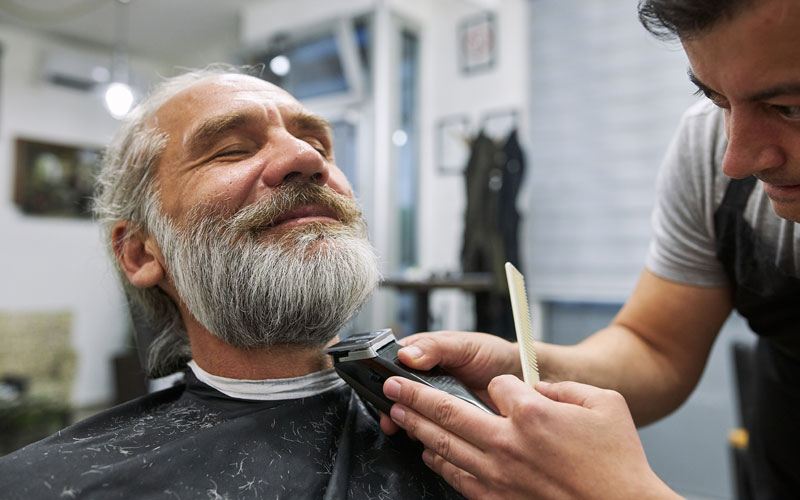 barber-salon Barber trims smiling mans beard at a salon with a trimmer and comb.