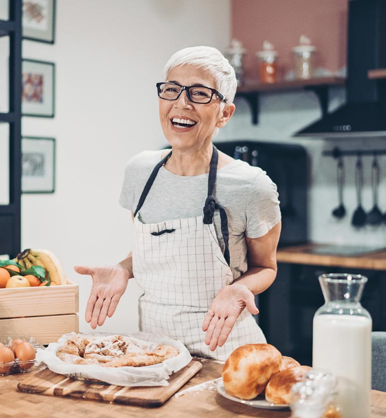 senior-baking An elderly woman with grey hair and glasses smiling proudly at her freshly baked pastries in the kitchen.