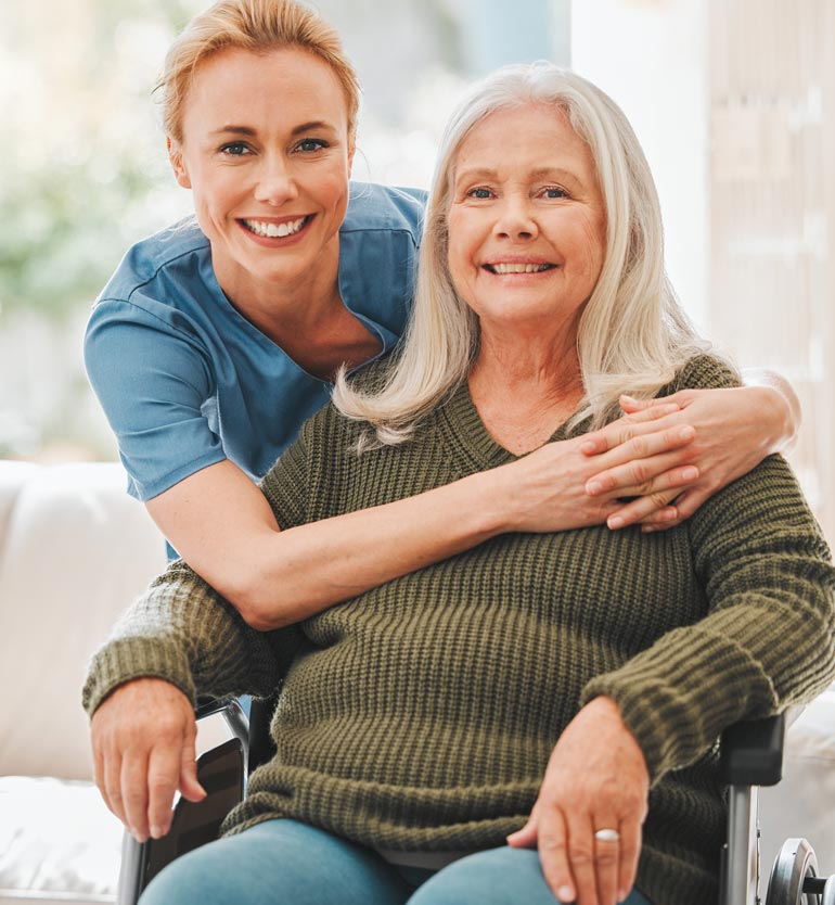 senior-healthcare A cheerful caregiver hugging a smiling senior woman in a wheelchair, showcasing compassionate care.