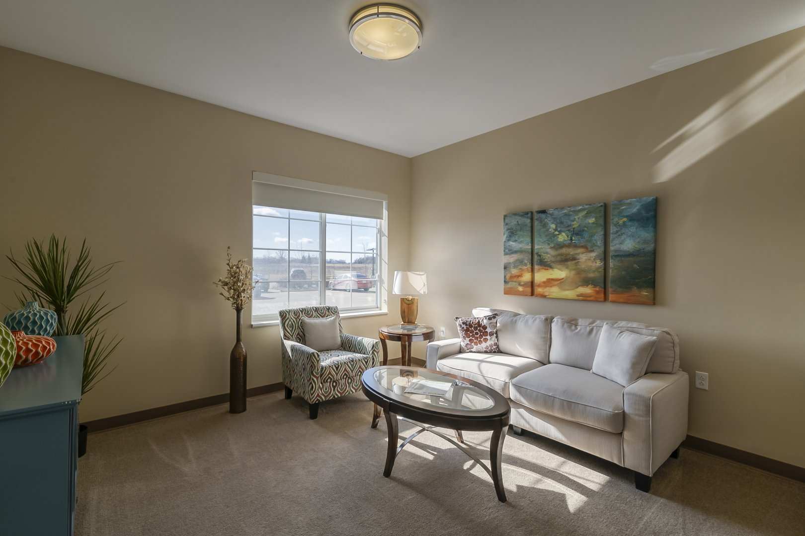 Modern living room with a white sofa, colorful armchair, glass coffee table, and wall art.