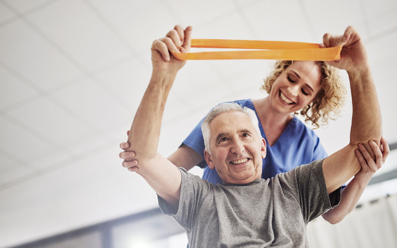 senior-wellness Senior man doing resistance band exercise with assistance from a healthcare worker