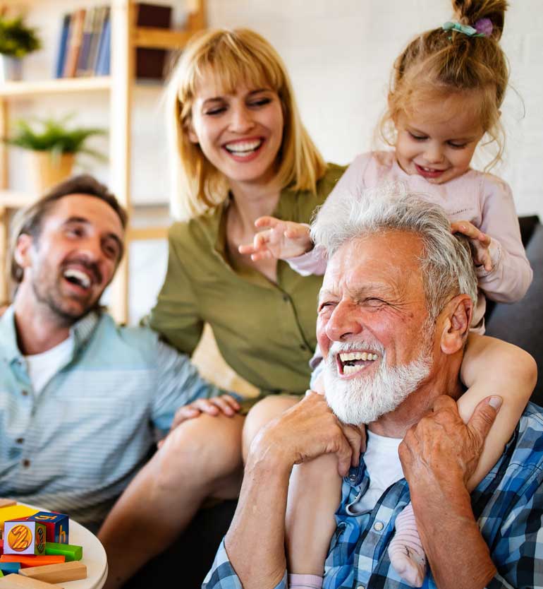 senior-with-family Senior man joyfully playing with family, including young child on his shoulders, laughing together.