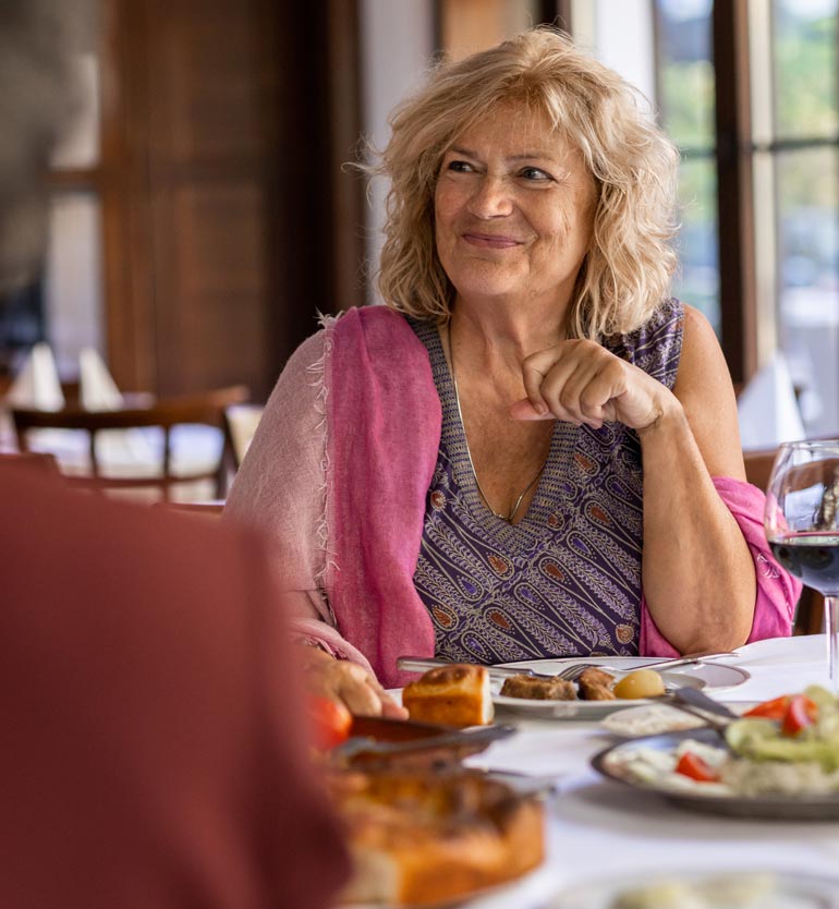 senior-friends-eating Senior woman smiling and dining with friends in a restaurant, enjoying a meal and conversation.