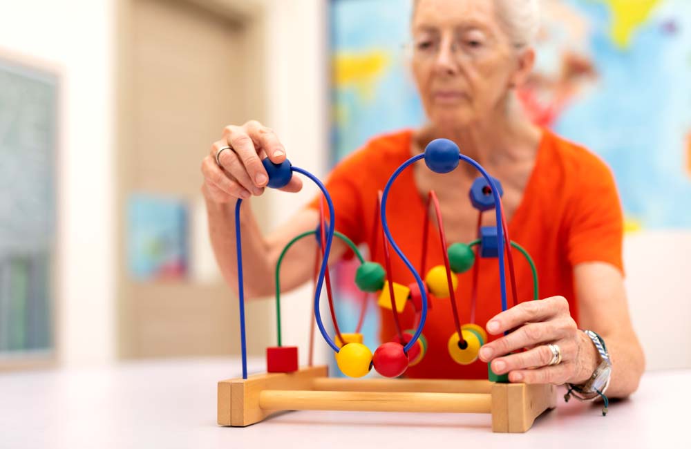 senior-memory-care--activity Senior woman engaging in a cognitive activity with a bead maze toy during a memory care session.