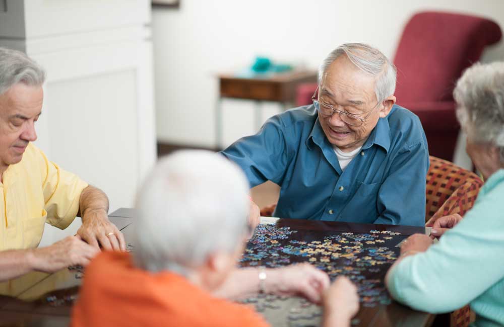 seniors-doing-puzzle Seniors sitting at a table, enjoying assembling a puzzle together in a relaxed environment.