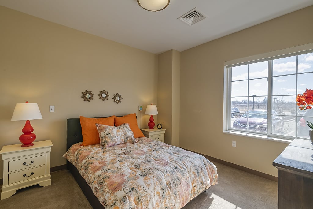 Large bedroom with orange accents and big windows.