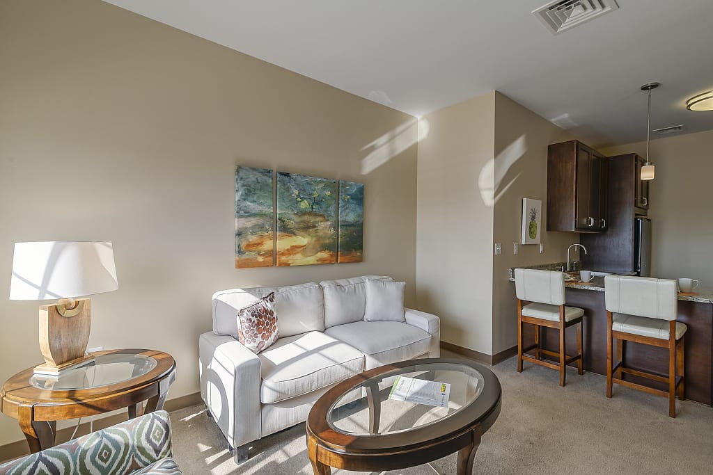 Cozy living area with open concept kitchen, featuring a large painting, barstools at the counter, and various decor.