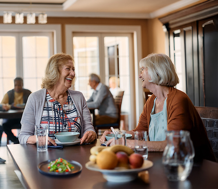 senior-women-friends-laughing-at-breakfast two female seniors laughing at breakfast table